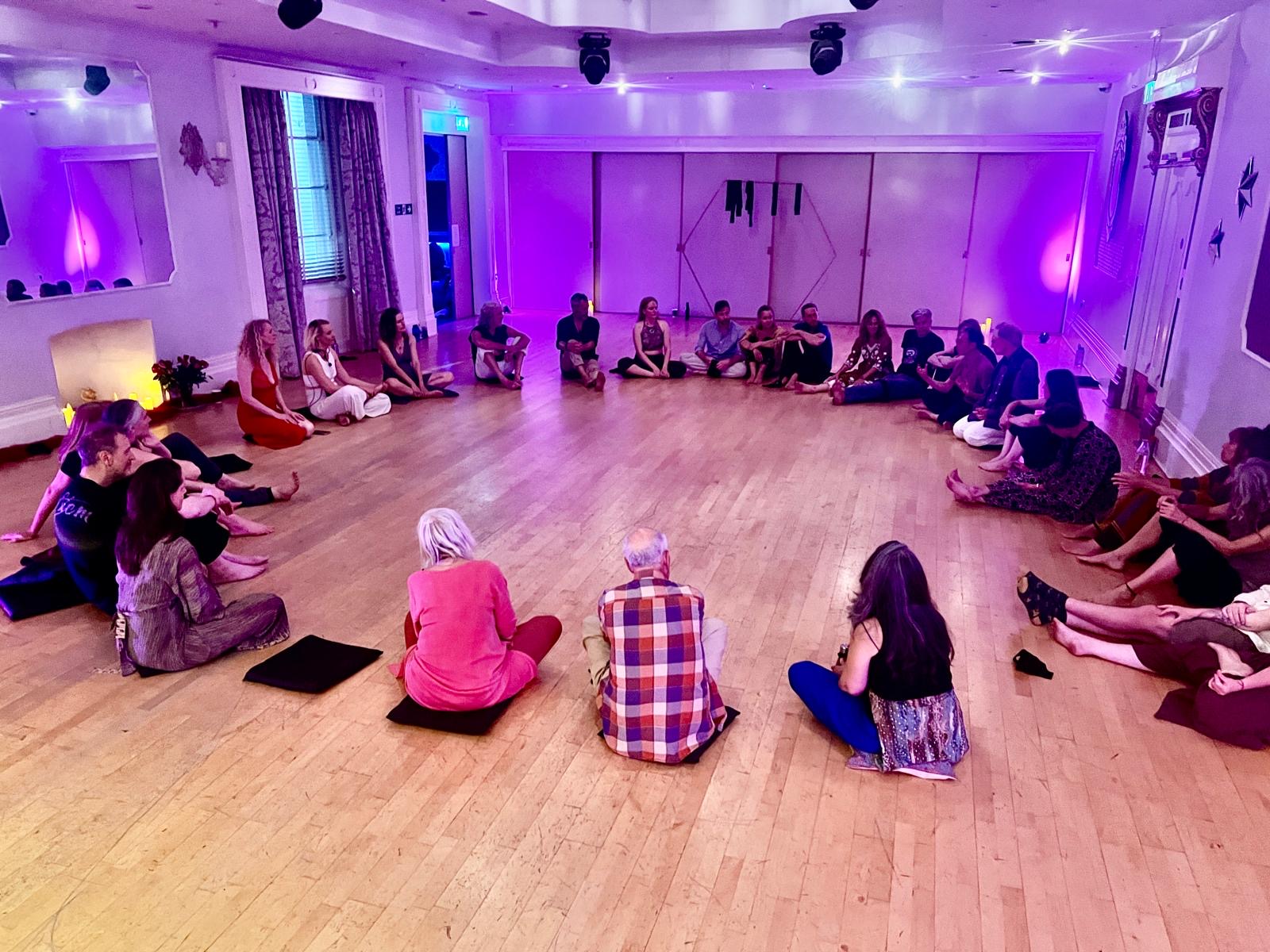 Everyone seated together on the floor in a large circle, listening and sharing