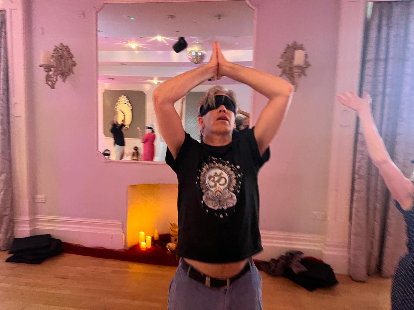 A blindfolded participant with hands joined high above his head